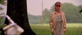 Movie still from “Kalifornia” (1993), directed by Dominic Sena – A woman standing next to a tree in a field; Medium shot, Low angle