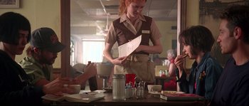 Movie still from “Kalifornia” (1993), directed by Dominic Sena – A woman standing at a table holding a menu; Medium shot, Over the shoulder angle