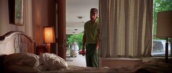 Movie still from “Kalifornia” (1993), directed by Dominic Sena – A man standing in front of a bed in a hotel room; Medium shot, Over the shoulder angle