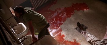 Movie still from “Kalifornia” (1993), directed by Dominic Sena – A man standing in a room with blood on the floor; Wide shot, Overhead angle