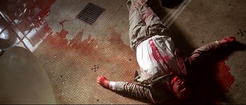 Movie still from “Kalifornia” (1993), directed by Dominic Sena – A man is laying on the floor with blood on his face; Wide shot, Overhead angle