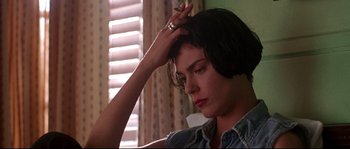 Movie still from “Kalifornia” (1993), directed by Dominic Sena – A woman sitting in front of a window holding her hand up to her head; Close Up shot, Low angle