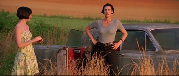 Movie still from “Kalifornia” (1993), directed by Dominic Sena – A woman standing next to a pile of suitcases in a field; Medium shot, Low angle