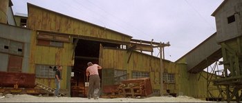 Movie still from “Kalifornia” (1993), directed by Dominic Sena – A man standing in front of an open door of a building; Extreme Wide shot, Low angle