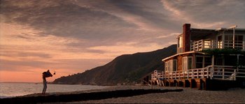 Movie still from “Kalifornia” (1993), directed by Dominic Sena – A house on the beach at sunset with mountains in the background; Extreme Wide shot, Low angle