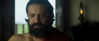 Movie still from “Kantara” (2022), directed by Rishab Shetty – A man with a beard and a necklace; Close Up shot, Low angle