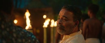Movie still from “Kantara” (2022), directed by Rishab Shetty – A person wearing a white shirt near candles; Close Up shot, Over the shoulder angle