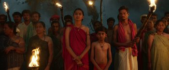 Movie still from “Kantara” (2022), directed by Rishab Shetty – A group of people standing in front of a tree with torches in their hands; Medium shot, Low angle