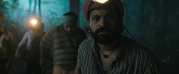 Movie still from “Kantara” (2022), directed by Rishab Shetty – A man with a beard and a red turban is looking at the camera; Close Up shot, Low angle