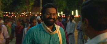 Movie still from “Kantara” (2022), directed by Rishab Shetty – A man with a long beard wearing a blue shirt and a yellow ribbon around his neck; Close Up shot, Over the shoulder angle