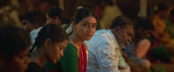 Movie still from “Kantara” (2022), directed by Rishab Shetty – A woman in a green sari is sitting in front of other people; Close Up shot, Over the shoulder angle