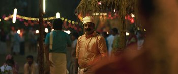 Movie still from “Kantara” (2022), directed by Rishab Shetty – A man wearing a turban standing in front of a crowd of onlookers; Medium shot, Over the shoulder angle