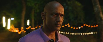 Movie still from “Kantara” (2022), directed by Rishab Shetty – A bald man in a purple shirt is looking at the camera; Close Up shot, Over the shoulder angle