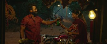 Movie still from “Kantara” (2022), directed by Rishab Shetty – A man and a woman are exchanging a drink; Medium shot, Over the shoulder angle