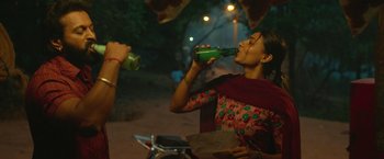 Movie still from “Kantara” (2022), directed by Rishab Shetty – A woman is drinking a drink from a green bottle; Medium shot, Low angle