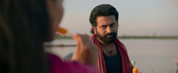 Movie still from “Kantara” (2022), directed by Rishab Shetty – A man with long hair and a beard standing next to a woman; Close Up shot, Over the shoulder angle