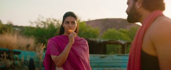 Movie still from “Kantara” (2022), directed by Rishab Shetty – A woman in a pink sari eating an orange; Medium shot, Over the shoulder angle
