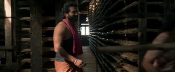Movie still from “Kantara” (2022), directed by Rishab Shetty – A man with a beard is standing in a room; Medium shot, Low angle