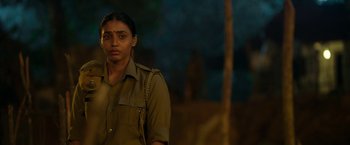 Movie still from “Kantara” (2022), directed by Rishab Shetty – A woman in a uniform standing in front of a tree; Close Up shot, Over the shoulder angle