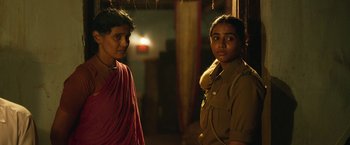 Movie still from “Kantara” (2022), directed by Rishab Shetty – Two women standing next to each other in a dark room; Medium shot, Over the shoulder angle