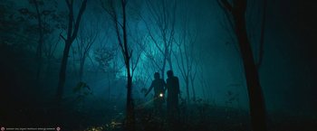 Movie still from “Kantara” (2022), directed by Rishab Shetty – Two people are standing in the woods at night with a flashlight; Extreme Wide shot, Low angle