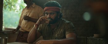 Movie still from “Kantara” (2022), directed by Rishab Shetty – A man with a beard is holding a glass of beer; Close Up shot, Low angle