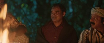 Movie still from “Kantara” (2022), directed by Rishab Shetty – A man wearing a red shirt and a black jacket; Close Up shot, Over the shoulder angle
