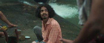 Movie still from “Kantara” (2022), directed by Rishab Shetty – A man sitting on the side of a body of water; Medium shot, High angle