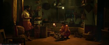 Movie still from “Kantara” (2022), directed by Rishab Shetty – A woman is cooking in an old fashioned kitchen; Wide shot, High angle
