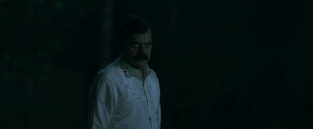 Movie still from “Kantara” (2022), directed by Rishab Shetty – A man in a white shirt is standing in the dark; Medium shot, Low angle