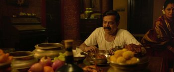 Movie still from “Kantara” (2022), directed by Rishab Shetty – A man sitting at a table with a plate of food; Medium shot, High angle