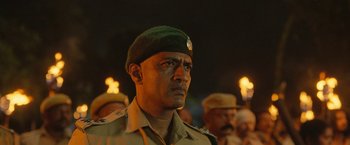 Movie still from “Kantara” (2022), directed by Rishab Shetty – A man in a green hat and a crowd of people; Close Up shot, Low angle