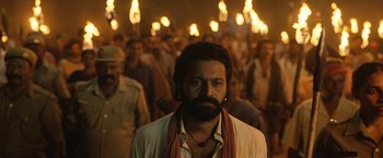 Movie still from “Kantara” (2022), directed by Rishab Shetty – A man with a beard is standing in front of a group of people; Medium shot, Low angle