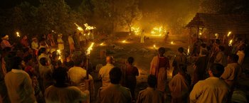 Movie still from “Kantara” (2022), directed by Rishab Shetty – A group of people standing in front of burning trees; Extreme Wide shot, High angle