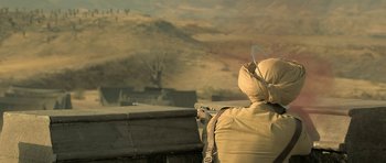 Movie still from “Kesari” (2019), directed by Anurag Singh – A person in a desert area holding a gun; Medium shot, Over the shoulder angle