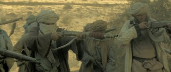 Movie still from “Kesari” (2019), directed by Anurag Singh – A man holding a rifle while standing next to another man; Medium shot, Over the shoulder angle
