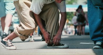 Movie still from “Kids” (1995), directed by Larry Clark – A man is tying his shoes on the sidewalk; Wide shot, Low angle