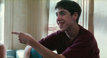Movie still from “Kids” (1995), directed by Larry Clark – A young man sitting on a couch smiling; Close Up shot, Over the shoulder angle