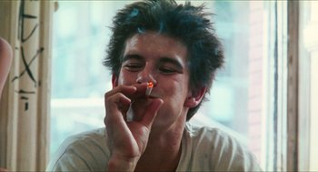 Movie still from “Kids” (1995), directed by Larry Clark – A young man smoking a cigarette in front of a window; Close Up shot, Low angle