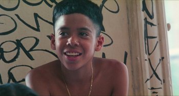 Movie still from “Kids” (1995), directed by Larry Clark – A young boy smiling for the camera with a gold chain around his neck; Close Up shot, Low angle