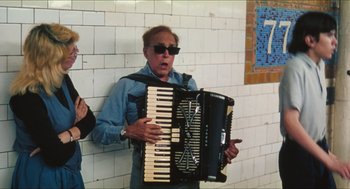 Movie still from “Kids” (1995), directed by Larry Clark – An older man holding an accordion in front of a brick wall; Medium shot, Low angle