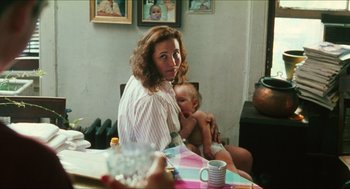 Movie still from “Kids” (1995), directed by Larry Clark – A woman sitting at a table with a baby in her lap; Medium shot, Over the shoulder angle