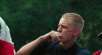 Movie still from “Kids” (1995), directed by Larry Clark – A young man is smoking a cigarette while sitting outside; Medium shot, Low angle