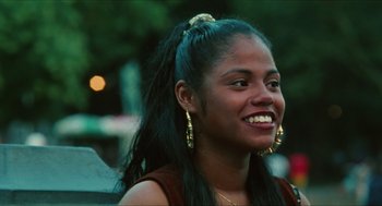 Movie still from “Kids” (1995), directed by Larry Clark – A young woman with long black hair smiles for the camera; Close Up shot, Over the shoulder angle