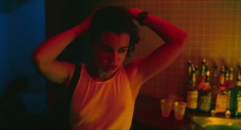 Movie still from “Kids” (1995), directed by Larry Clark – A young woman in a yellow shirt is holding her hands in her hair; Close Up shot, Over the shoulder angle