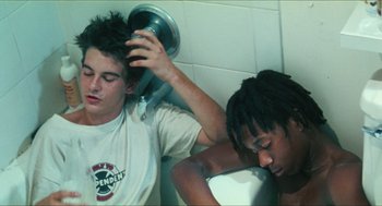 Movie still from “Kids” (1995), directed by Larry Clark – Two young men in a bathroom , one of whom has a hair dryer in his head; Medium shot, High angle
