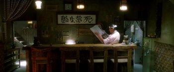 Movie still from “Kill Bill: Vol. 1” (2003), directed by Quentin Tarantino – A man sitting at a table reading a newspaper; Wide shot, Low angle