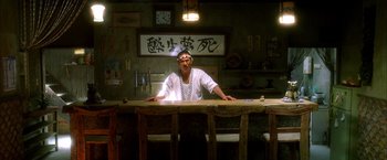 Movie still from “Kill Bill: Vol. 1” (2003), directed by Quentin Tarantino – A man sitting at a table in front of an oriental sign; Wide shot, Low angle