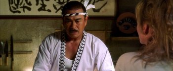 Movie still from “Kill Bill: Vol. 1” (2003), directed by Quentin Tarantino – A man in a white shirt and a chain around his neck; Close Up shot, Low angle