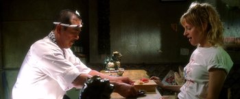 Movie still from “Kill Bill: Vol. 1” (2003), directed by Quentin Tarantino – A man in white shirt cutting a piece of pizza; Medium shot, Low angle